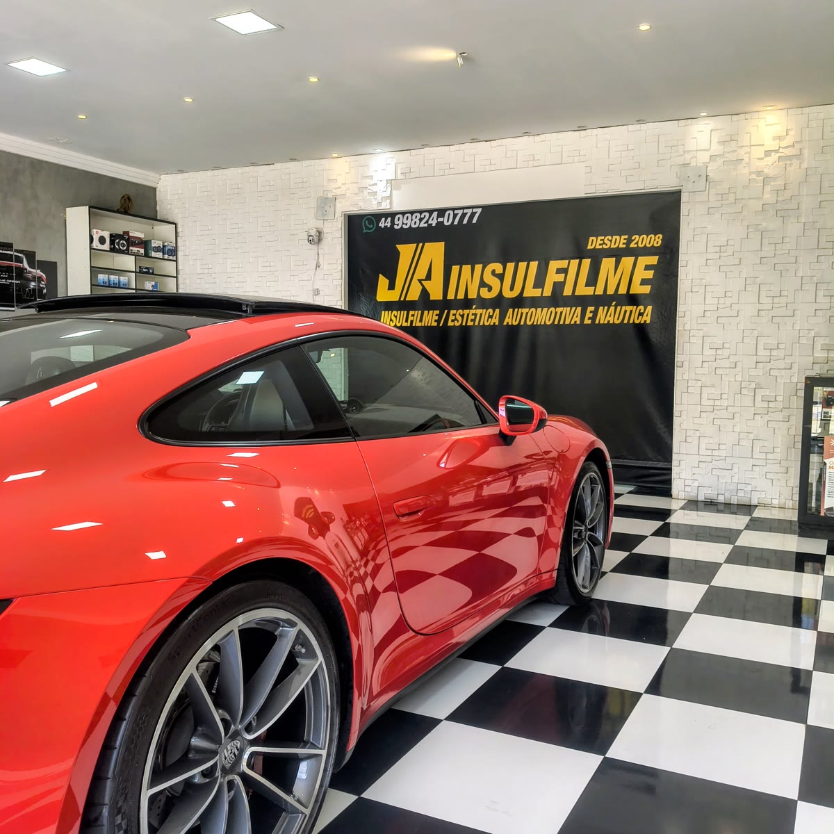 Carro esportivo vermelho dentro da JA Insulfilme, sobre o piso xadrez
